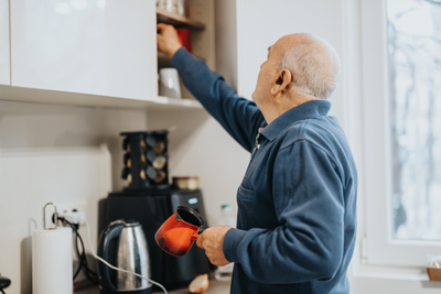 elderly man reaching for a kitchen cabinet holding a red coffee pot in a modern kitchen setting with appliances and natural light 14 ways to enjoy coffee