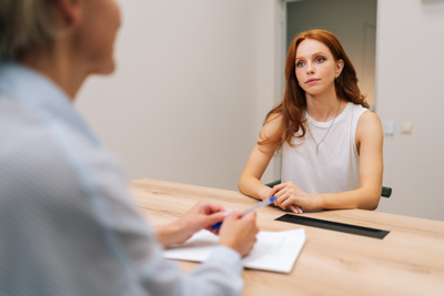 two women in a professional setting engaged in a conversation with focus on the woman sitting at the table discussing important topics related to a twelve step process