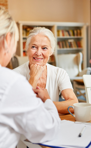 woman engaging in conversation with caregiver in a bright setting with coffee cup and books emphasizing 15 years of care